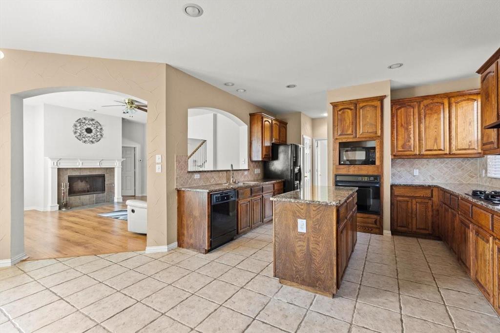 Kitchen featuring stained wood cabinetry, stone-finish countertops, a center island, recessed lighting, and tile flooring