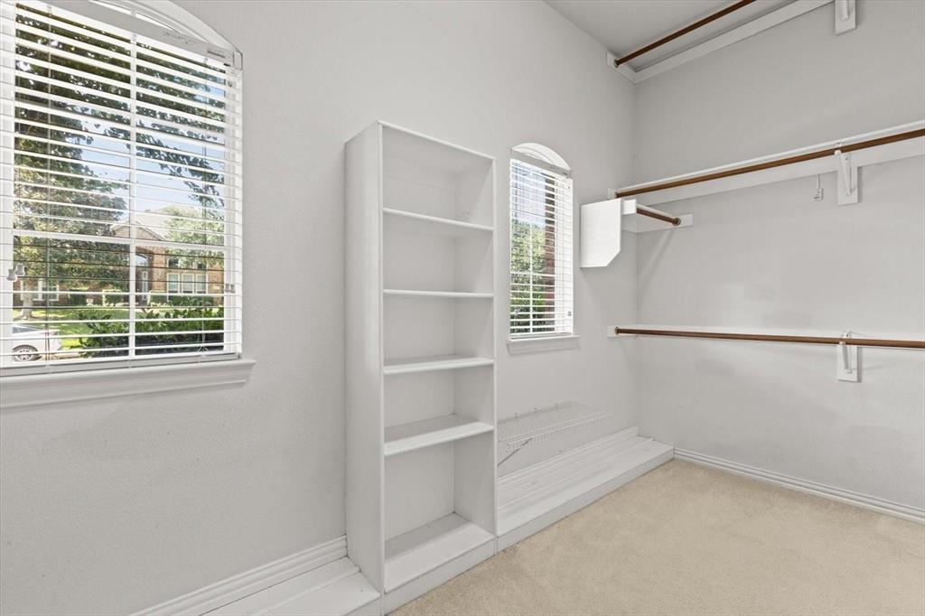 Walk-in closet featuring built-in shelving, dual-level hanging rods, and arched windows with horizontal blinds