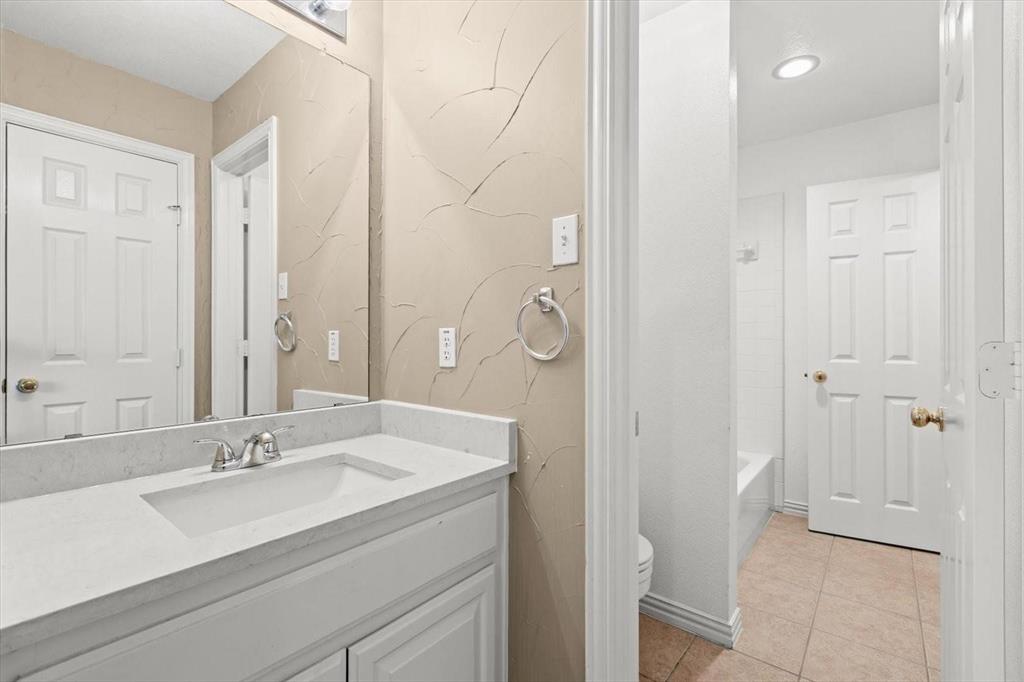 Bathroom vanity featuring white cabinetry, a light-toned solid surface countertop, an integrated rectangular basin, and a wall-to-wall mirror with textured wall finish