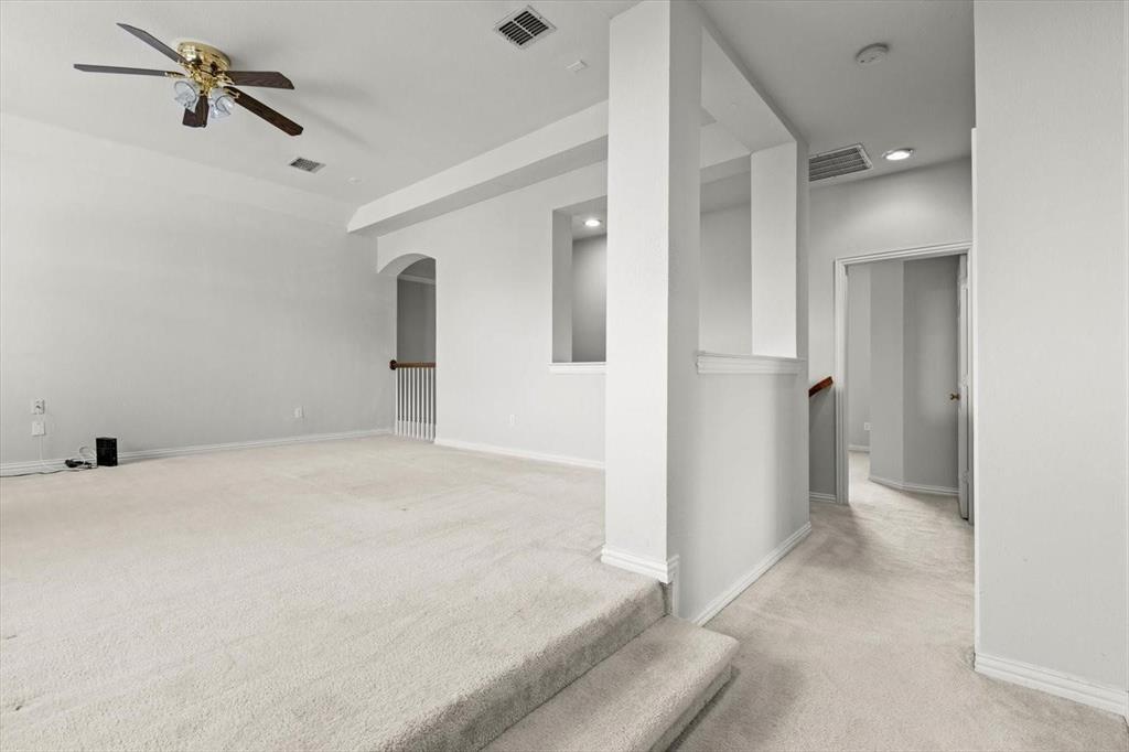 Multi-level room featuring wall-to-wall carpeting, elevated platform area, ceiling fan with light fixture, architectural cut-out wall, and staircase with wooden handrail
