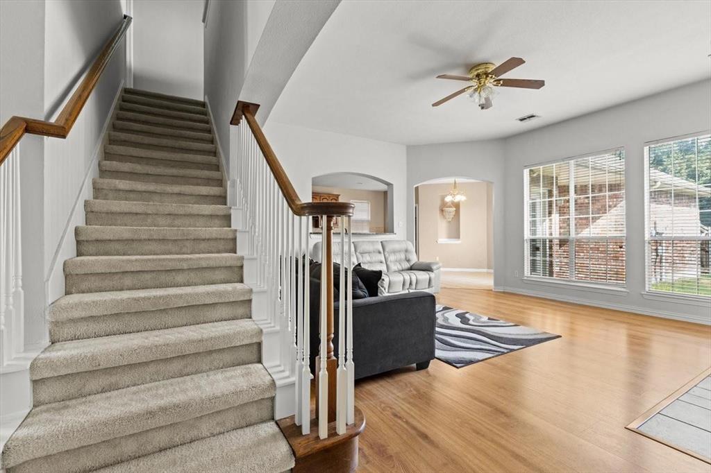 Staircase featuring carpeted steps, a wood-finish handrail, and white balusters, wooden-finish flooring, large windows, and a ceiling-mounted light fixture with a fan