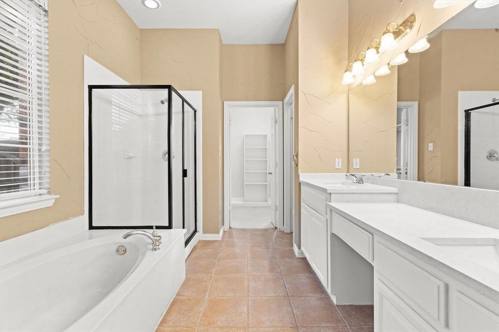 Bathroom featuring a dual-sink vanity with white cabinetry and solid-surface countertops, an oval soaking tub, a separate glass-enclosed shower, and tile flooring