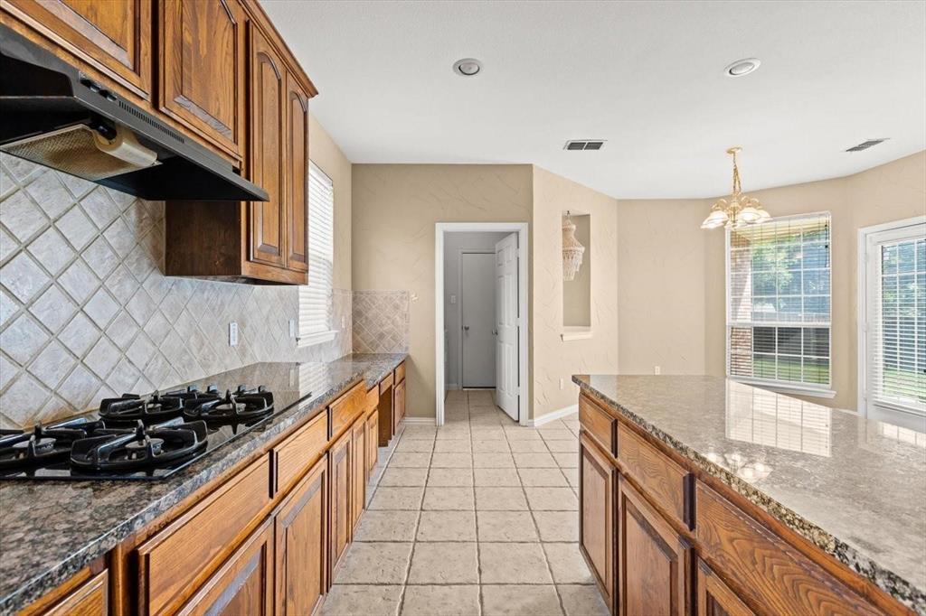 Kitchen featuring stained wood cabinetry, stone-finish countertops, diagonal tile backsplash, center island, and tile flooring