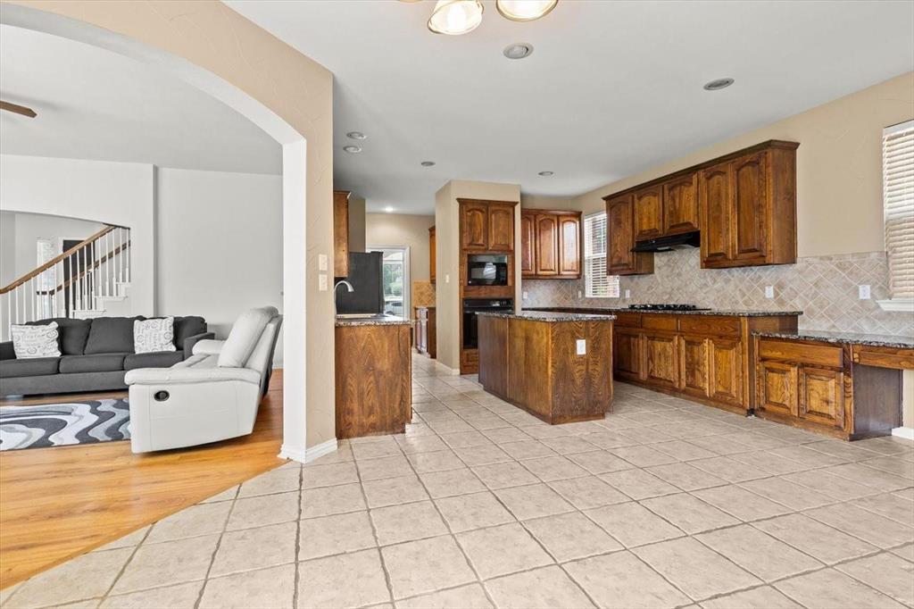 Kitchen featuring stained wood cabinetry, central island, stone-finish countertops, tiled backsplash, and recessed lighting