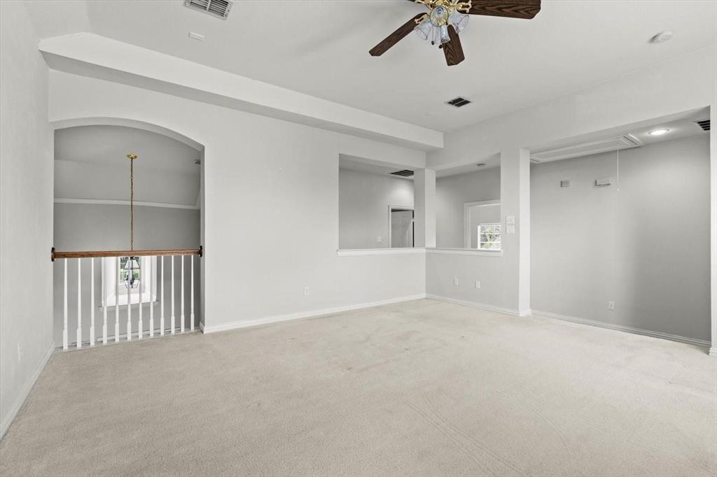 Vaulted ceilings, carpeted flooring, wall-cutout architectural features, ceiling fan with light fixture, and wooden baluster railing