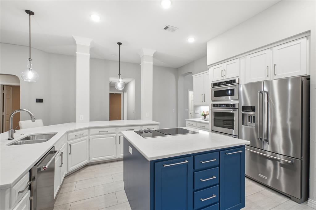 A chef-inspired kitchen with crisp white cabinetry, bright counters, glass pendant lights and a built-in wall oven and microwave. The deep navy island steals the show.