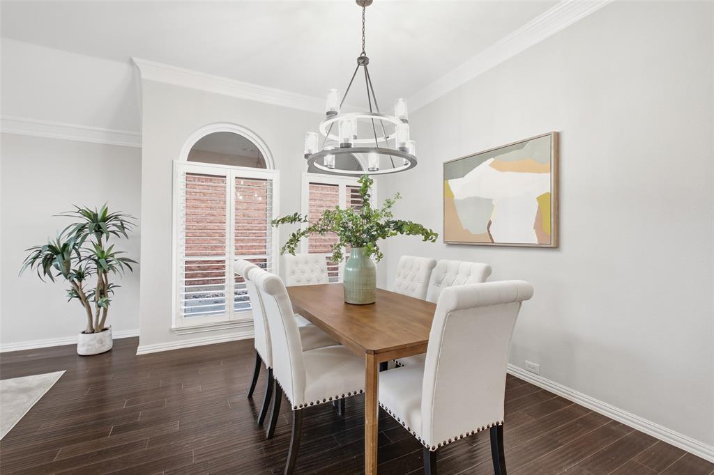 A formal dining room made for hosting, with a statement chandelier, plantation shutters on arched windows, and rich dark wood floors.