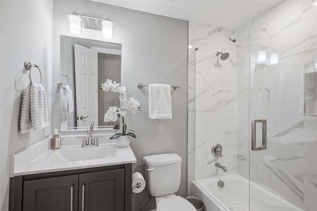 The updated guest bath is crisp and modern, with marble-look tile, a frameless glass enclosure and contemporary fixtures.