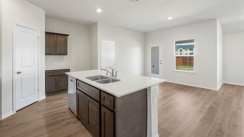 Kitchen island with integrated double basin sink, white countertops, dark wood-finish cabinetry, and wood-finish flooring