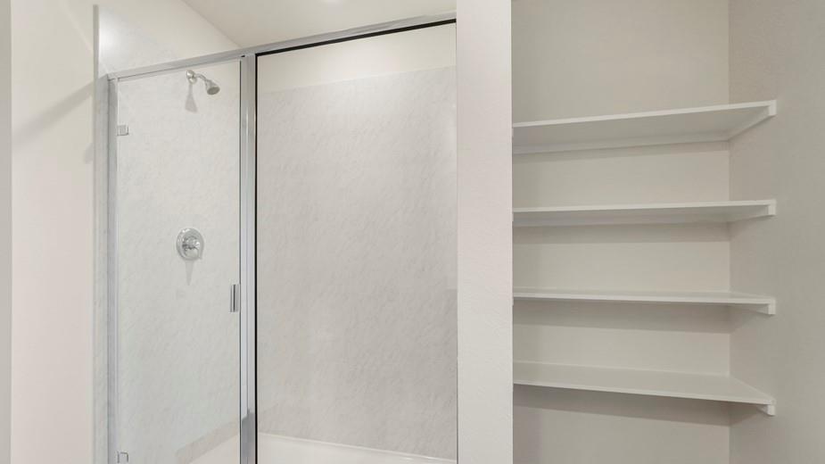 Shower enclosure with clear glass door, chrome showerhead, and circular control, accompanied by built-in shelving