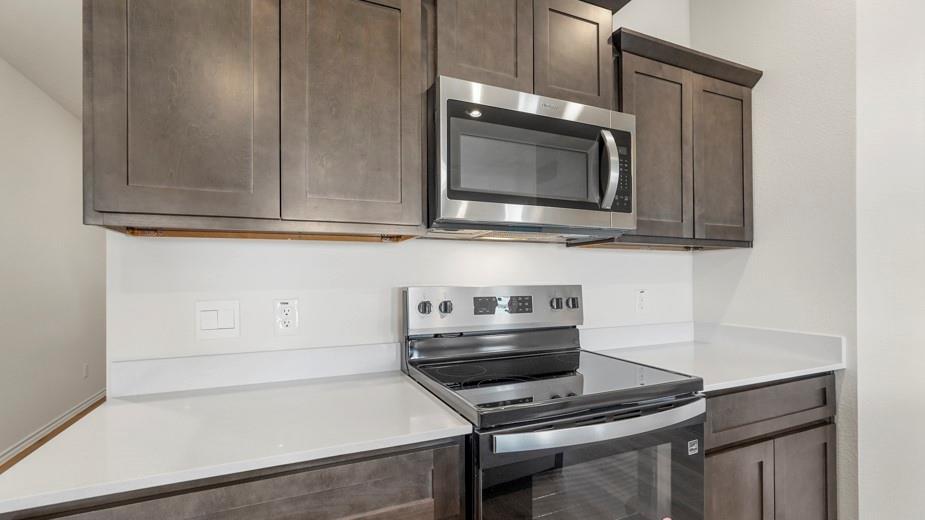 Gray shaker-style cabinetry with crown molding, stainless steel microwave, electric range, and light-toned countertops