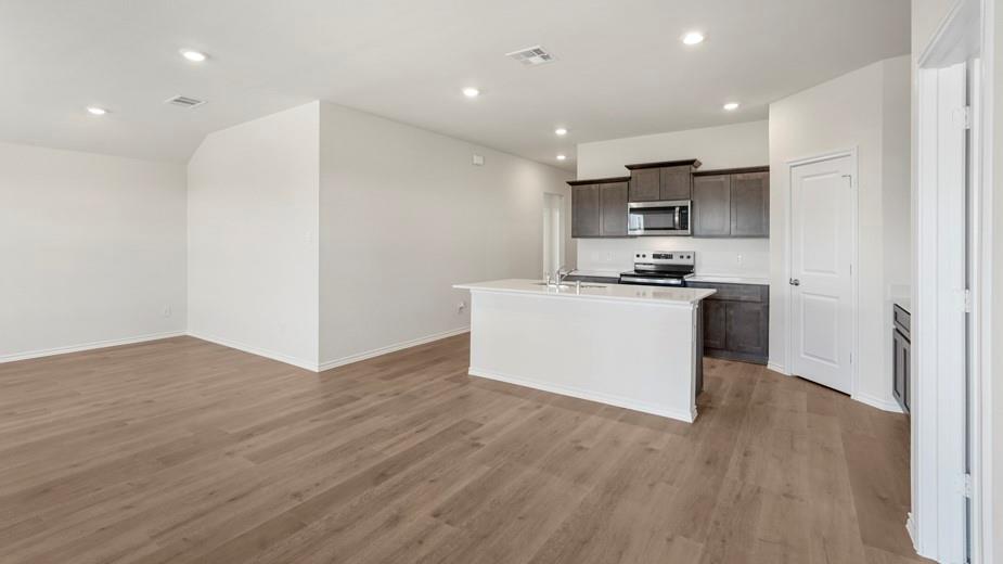 Expansive wood-finish flooring throughout, recessed lighting, kitchen island with built-in sink, dark wood cabinetry, and stainless steel appliances