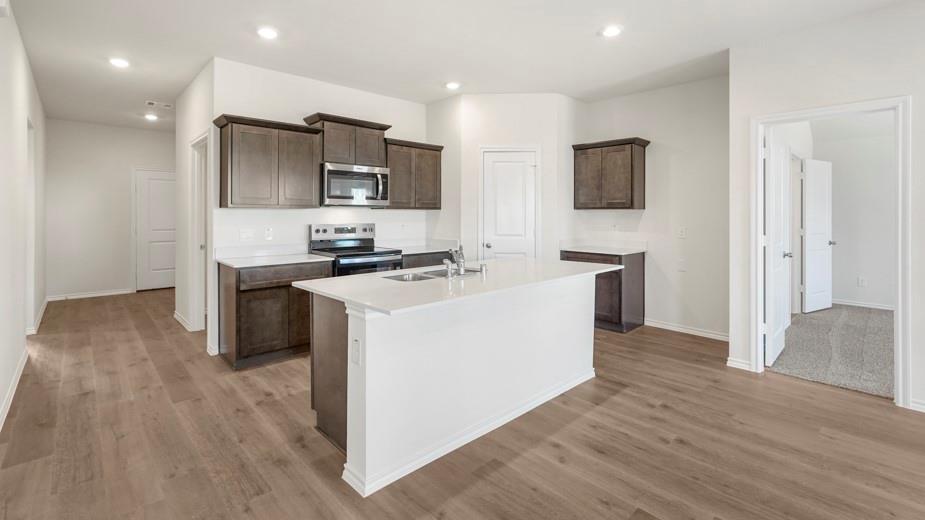 Kitchen featuring an island with a built-in sink, wood-finish flooring, recessed lighting, white countertops, and dark wood cabinetry