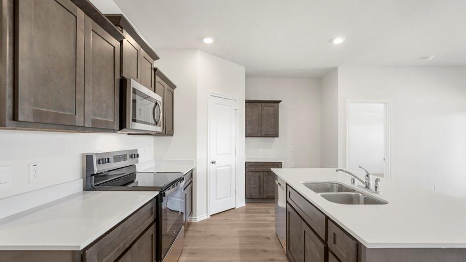 Kitchen featuring wood-finish flooring, white countertops, dark wood-finish cabinetry, stainless steel appliances, and an undermount double basin sink