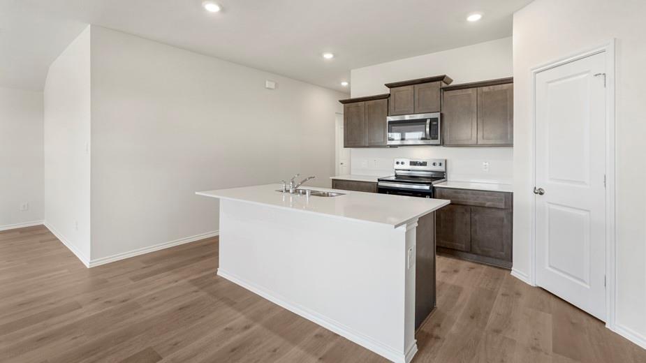 Kitchen with wood-finish flooring, dark wood cabinetry, stainless steel appliances, and a central island with a white countertop