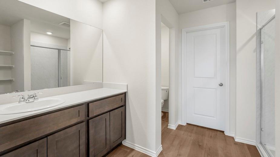 Single vanity with an integrated sink, polished chrome faucet, wood-finish cabinetry, and a large wall mirror