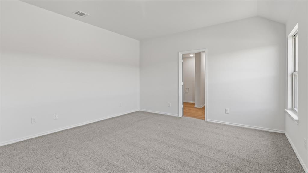 Spacious room featuring vaulted ceilings, light gray carpeting, and a window for natural illumination