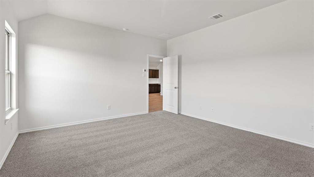 Spacious room featuring vaulted ceilings, light gray carpeting, white baseboards, and a white interior door