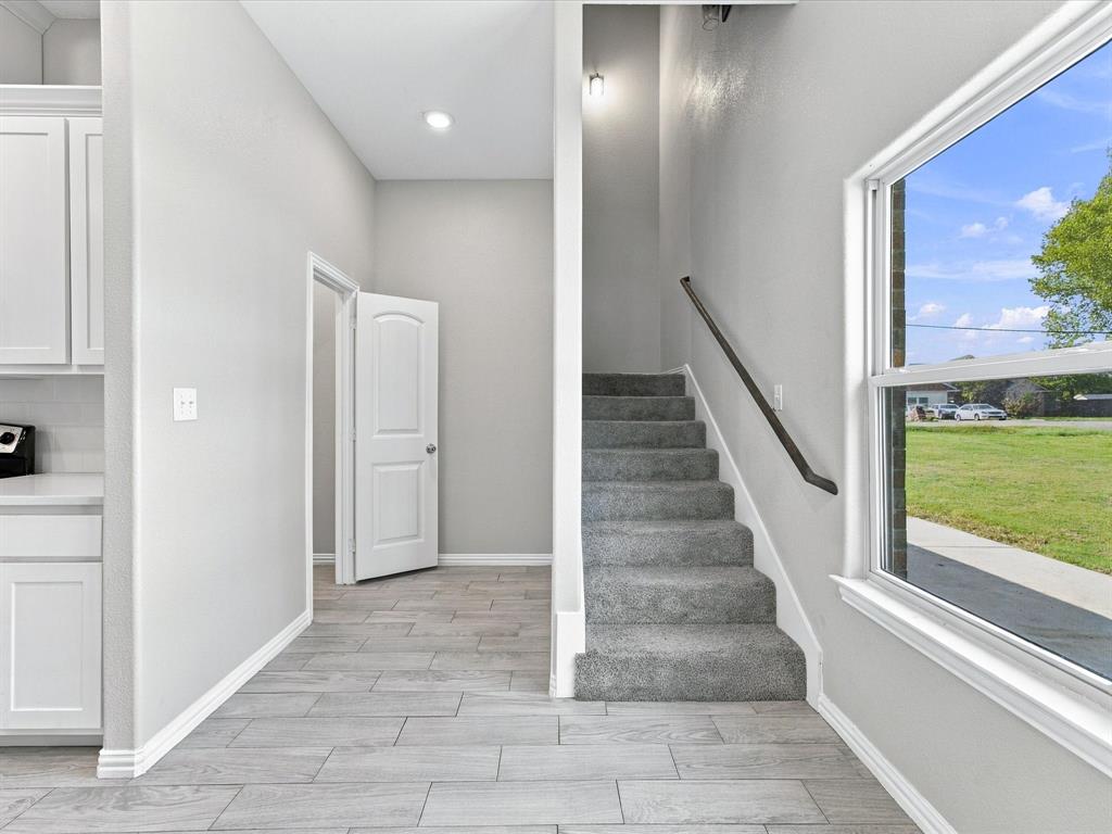 Interior space featuring wood-finish tile flooring, recessed lighting, carpeted staircase with a dark handrail, and large-format windows