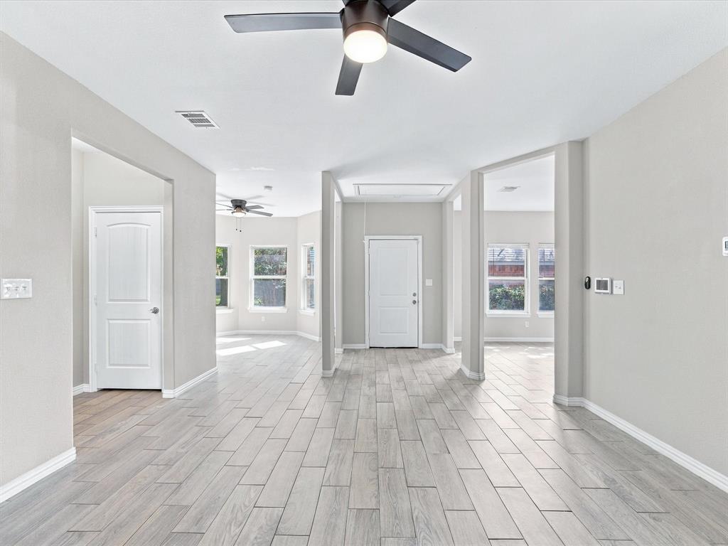 Interior space featuring wood-finish flooring, neutral wall paint, multi-blade ceiling fans with integrated lighting, and multiple windows with white trim