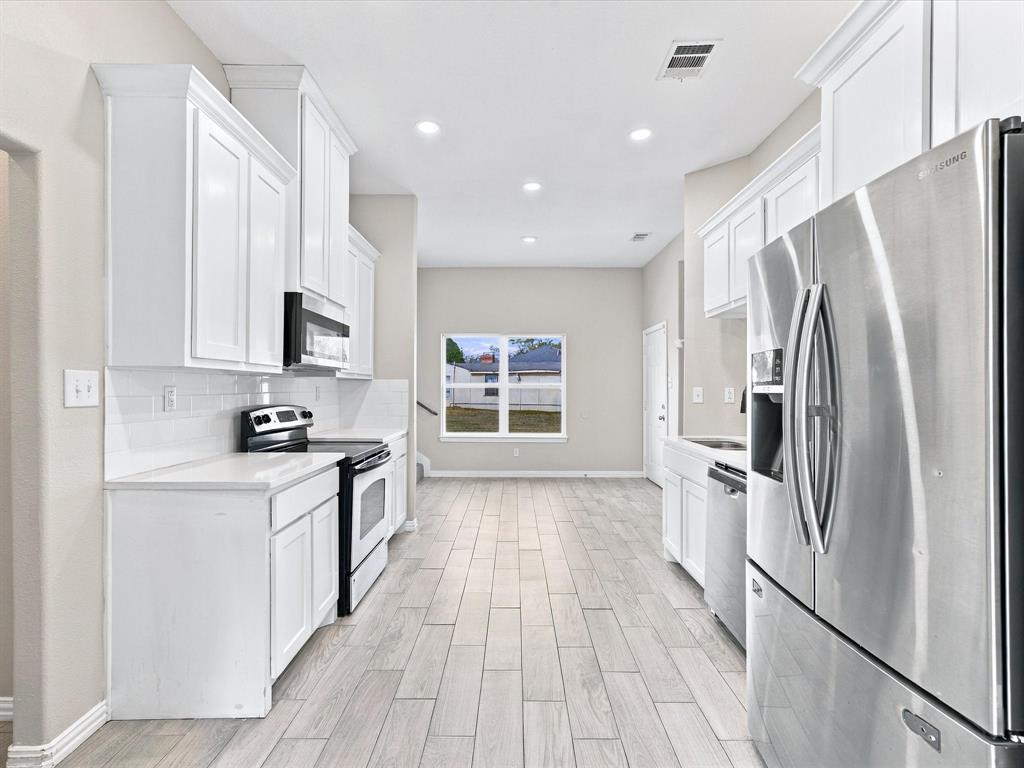Kitchen featuring white cabinetry, solid-surface countertops, subway tile backsplash, stainless steel appliances, and wood-finish tile flooring