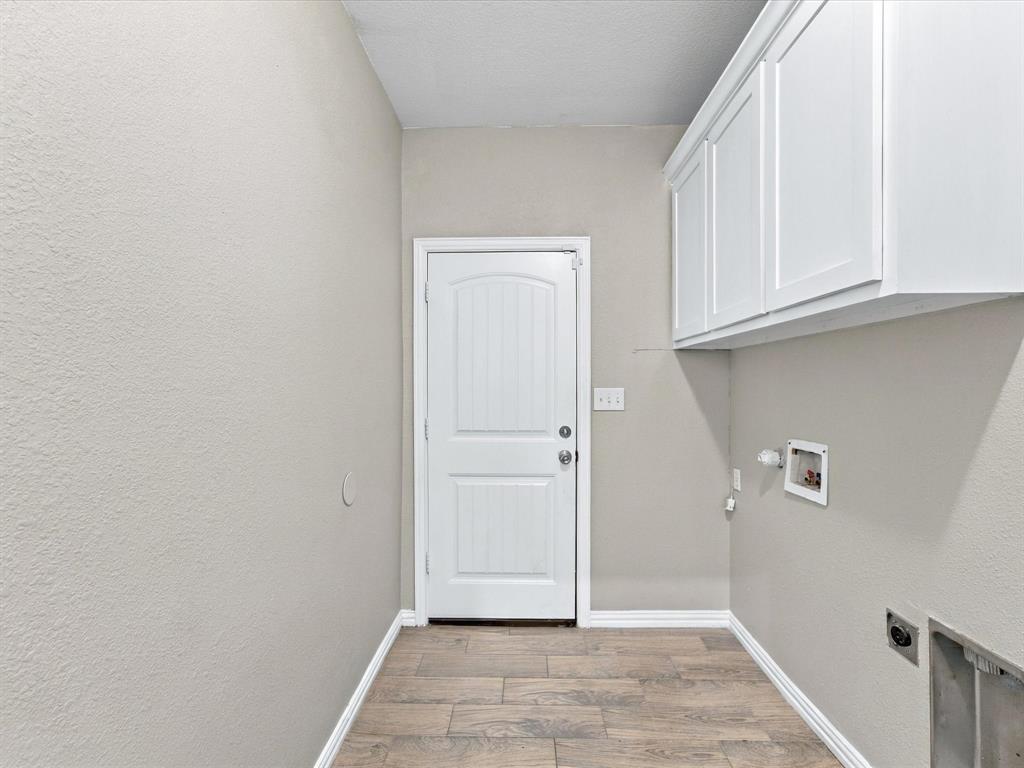 Utility area featuring wood-finish tile flooring, white shaker-style wall-mounted cabinetry, a solid-core entry door, and dedicated plumbing connections