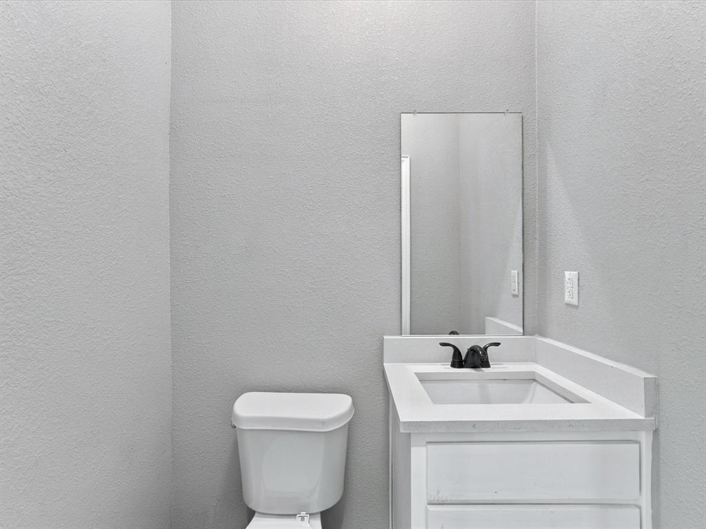 White vanity with rectangular integrated sink, neutral stone-composite countertop, matte black widespread faucet, and frameless wall-mounted mirror