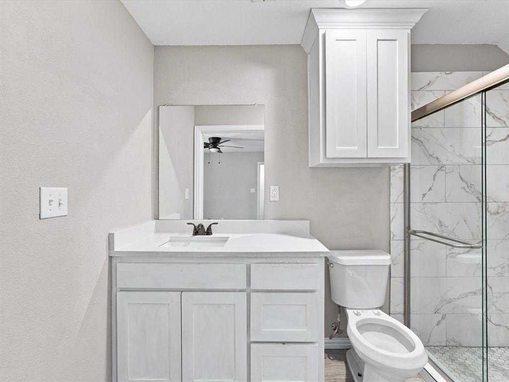Bathroom featuring a white vanity cabinet with an integrated countertop, recessed mirror, wall-mounted upper cabinetry, and a walk-in shower with glass enclosure