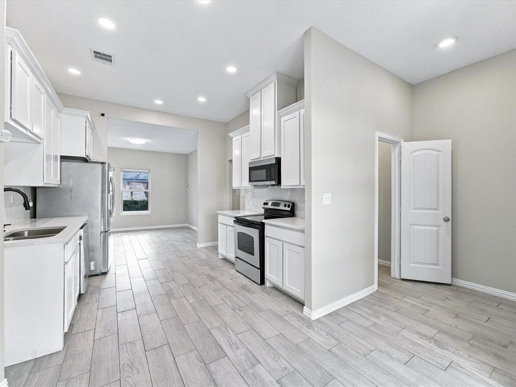Kitchen featuring white shaker-style cabinetry, stainless steel appliances, wood-finish tile flooring, recessed lighting, and solid-surface countertops