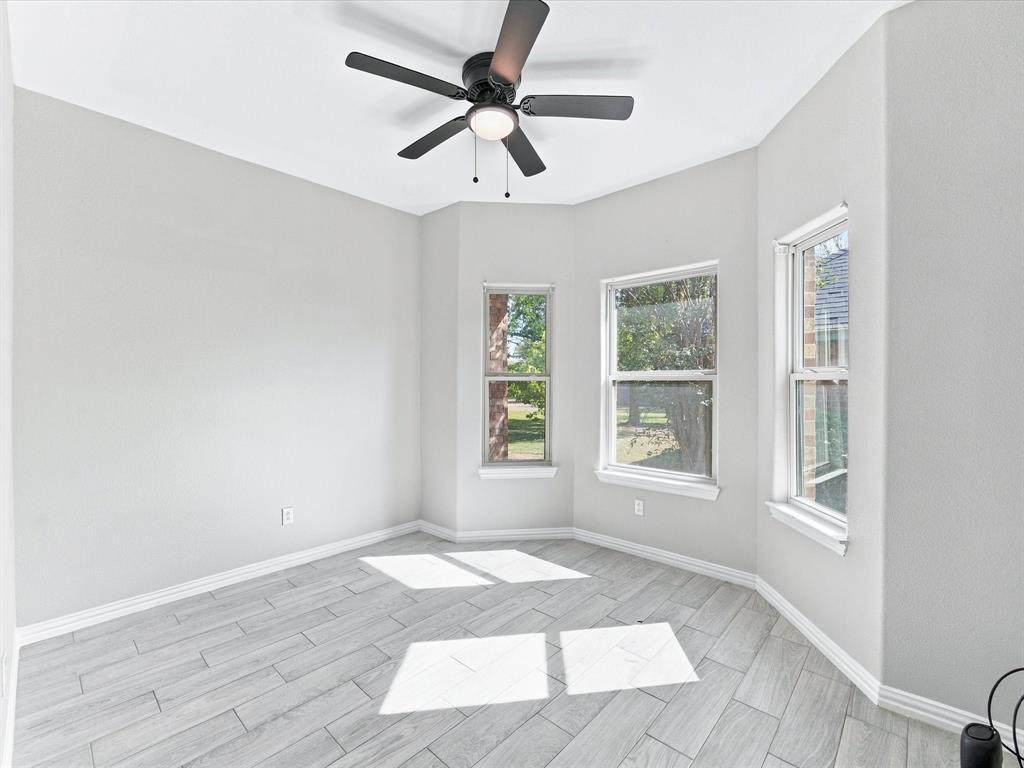 Interior space featuring neutral-toned walls, wood-finish tile flooring, three large windows, and a ceiling-mounted light fixture with a fan