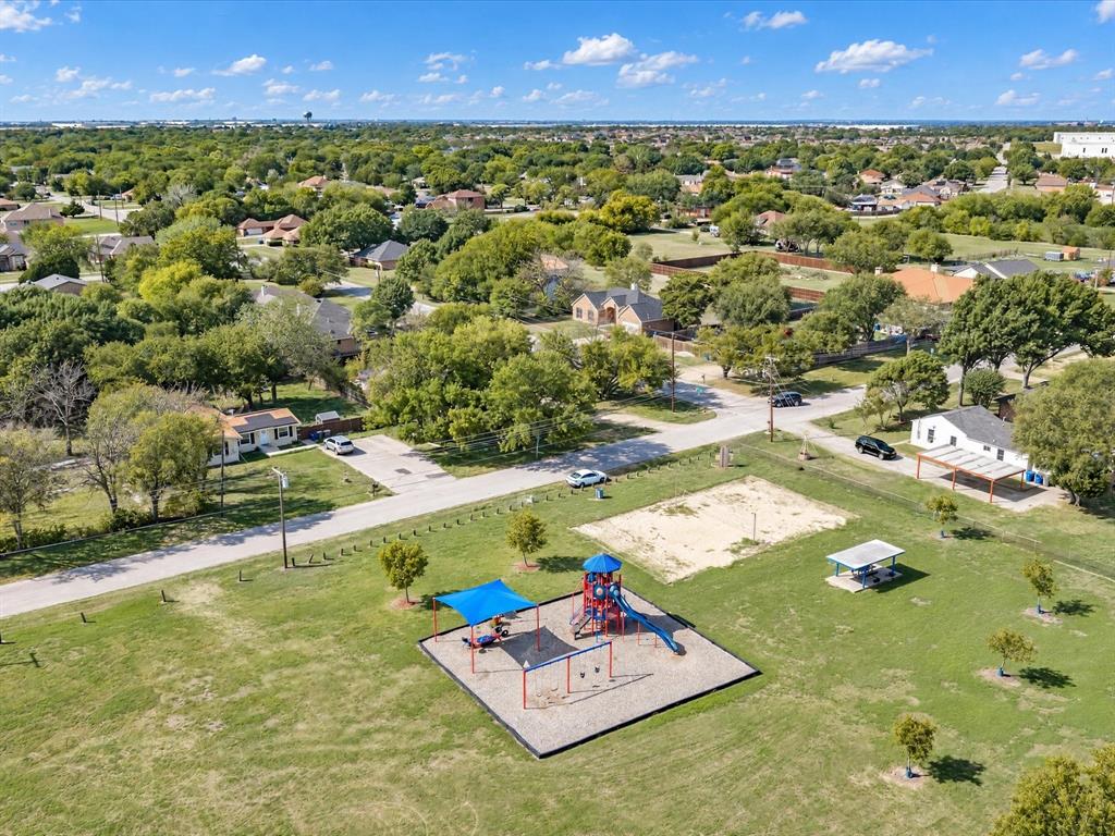 Expansive open green space featuring a playground with shade structures, a sand court, and a covered picnic area