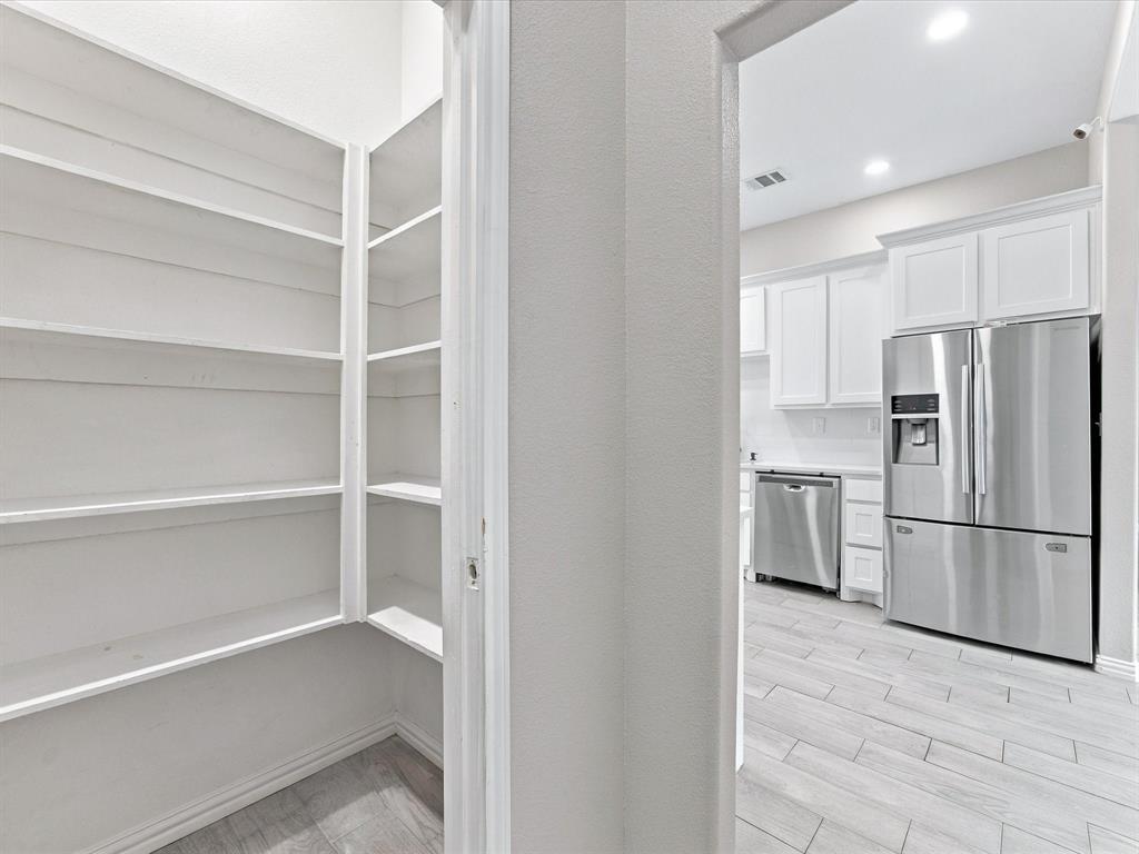 Walk-in pantry featuring built-in white shelving, tile flooring, stainless steel kitchen appliances, white cabinetry, and recessed lighting