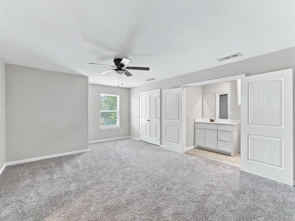 Upstairs secondary Primary Bedroom with neutral-toned interior featuring carpeted flooring, a ceiling fan with integrated lighting, multi-panel doors, and a vanity with a rectangular sink