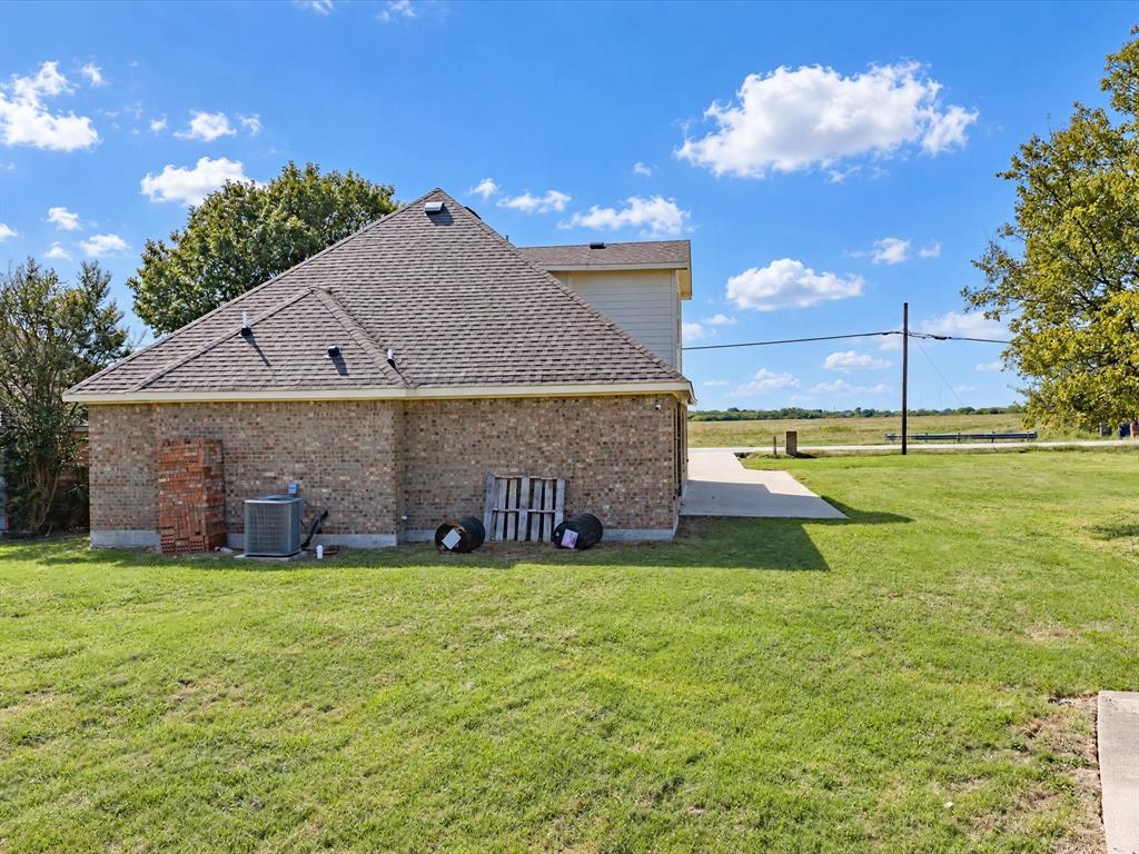 Exterior featuring a brick facade, composition shingle roof, concrete driveway, and expansive lawn area