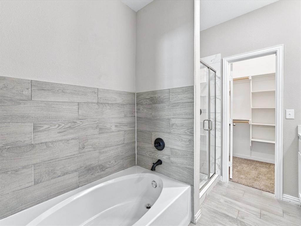 Soaking tub featuring wood-finish tile surround, separate glass-enclosed shower, matte black plumbing fixtures, and walk-in closet with built-in shelving