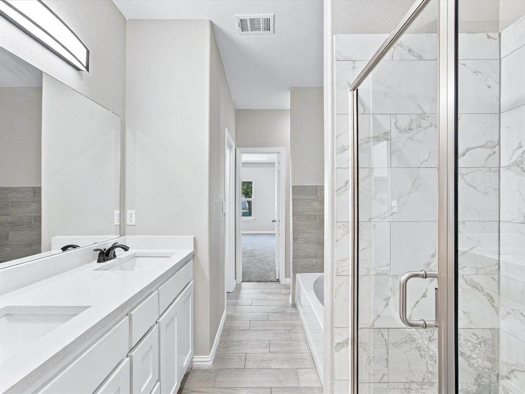 Bathroom featuring a dual-sink vanity with a white countertop, a walk-in shower with a glass enclosure and wall-tiling, a soaking tub, and tile flooring