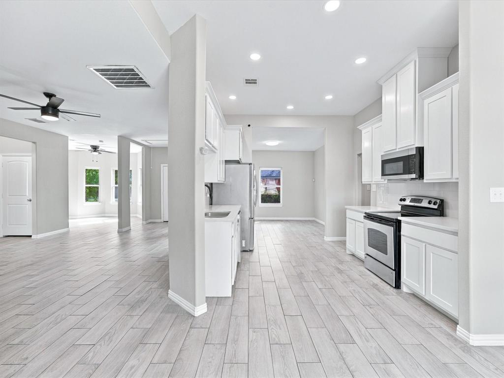 Kitchen featuring white cabinetry, stainless steel appliances, and solid surface countertops, complemented by recessed lighting and light-toned wood-finish flooring