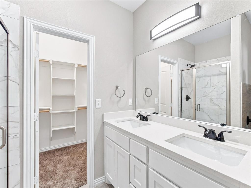Double vanity with white cabinetry, light-toned countertop, and matte black fixtures, paired with a full-width mirror and integrated lighting