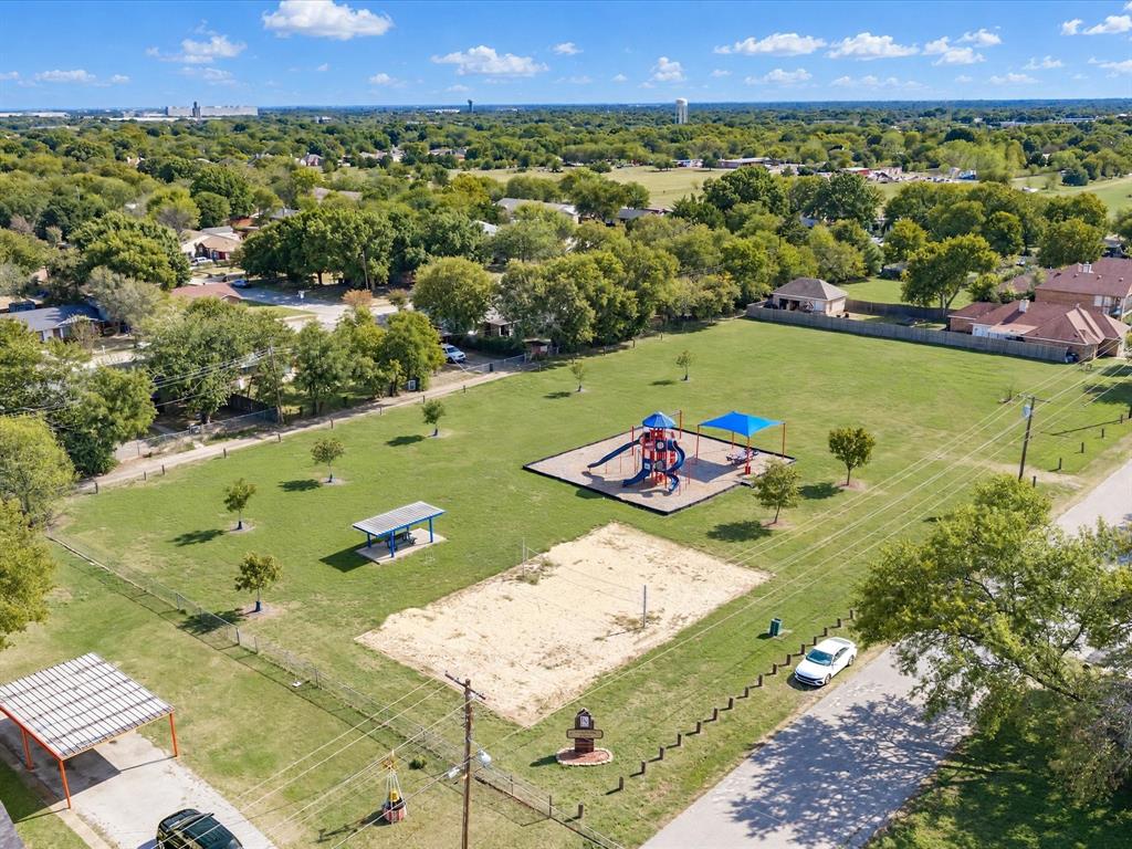 Expansive recreational area featuring a playground structure, sand volleyball court, shaded picnic pavilion, and mature trees across a manicured lawn