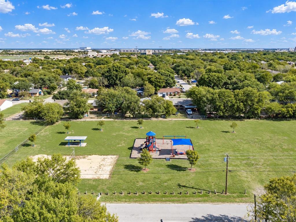 Expansive outdoor recreation space featuring a playground structure, sand volleyball court, and covered pavilion set within a landscaped lawn