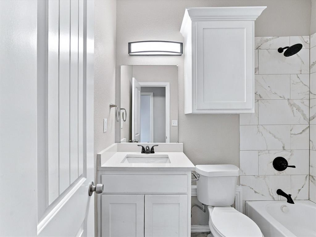 White vanity with a solid-surface countertop and undermount sink, matching wall-mounted cabinetry, tub-and-shower combination with large-format tile surround, and matte black plumbing fixtures