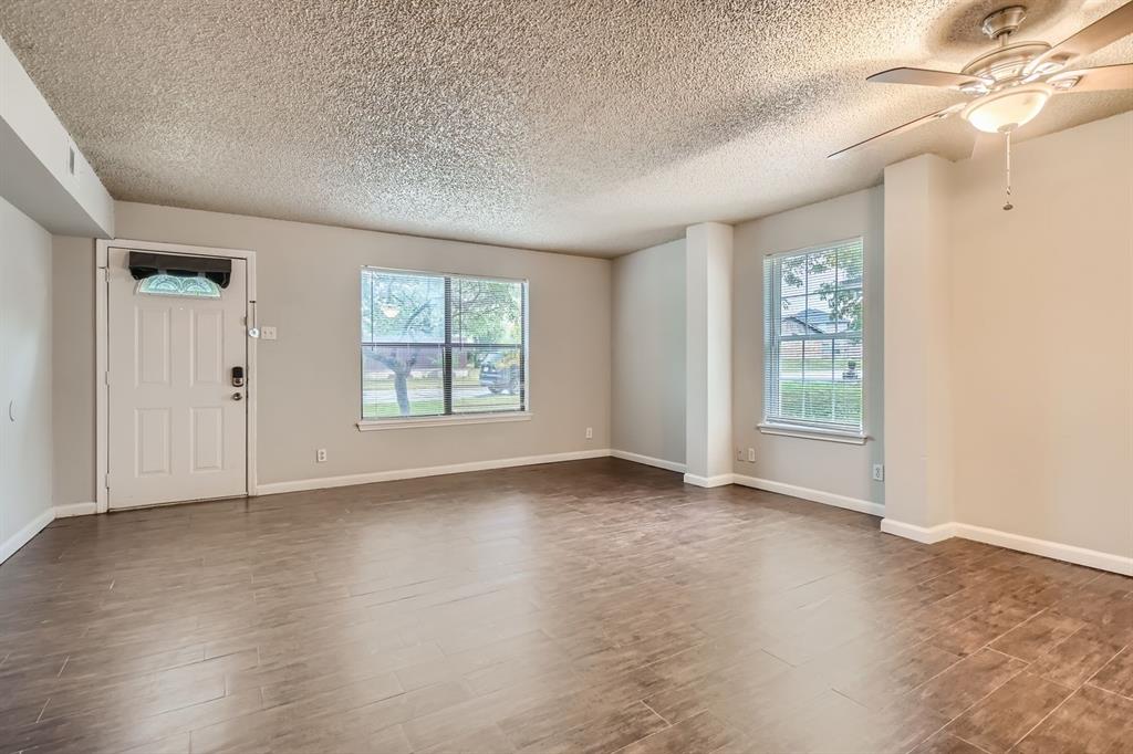 Living area featuring wood-finish tile flooring, a multi-blade ceiling fan with integrated lighting, dual windows, and a multi-panel entry door