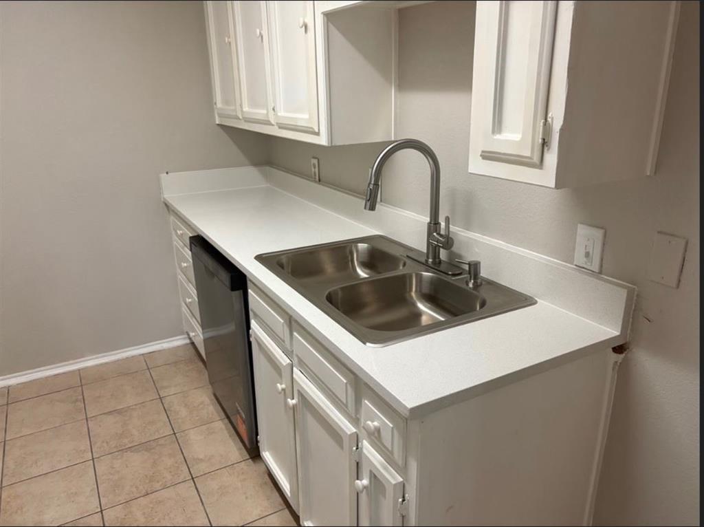 Kitchen featuring white cabinetry, solid-surface countertops, dual-basin stainless steel sink with high-arc pull-down faucet, and ceramic tile flooring