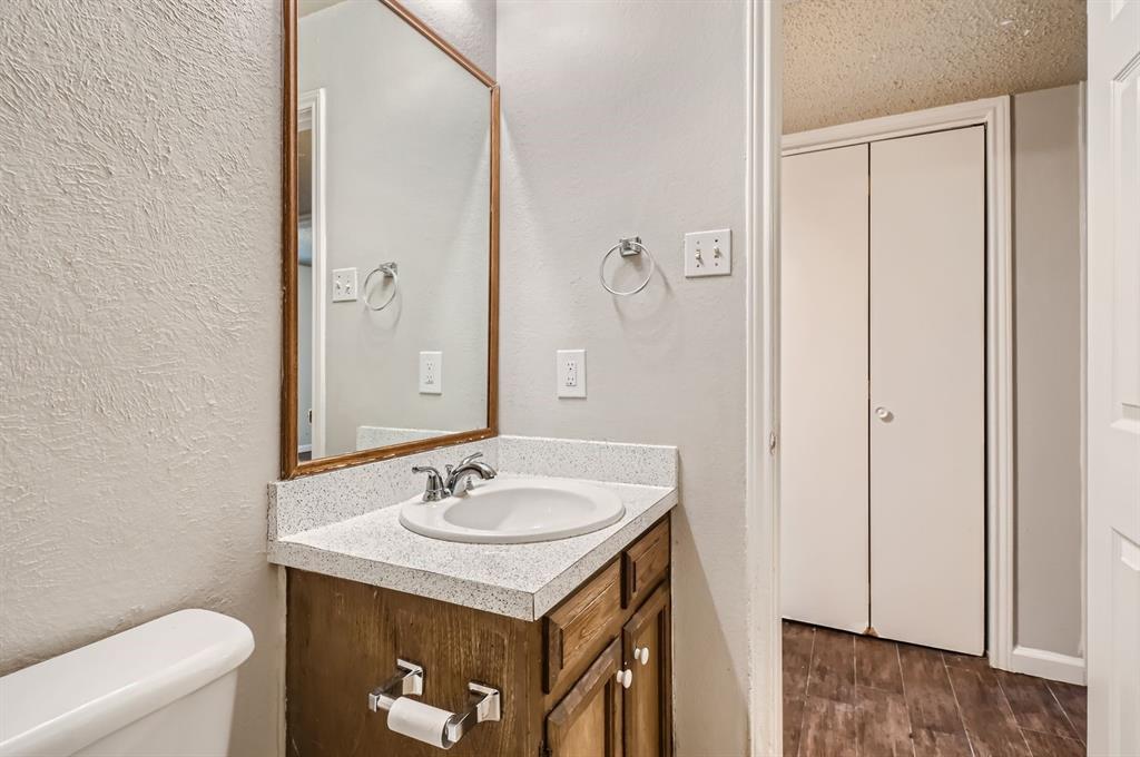 Wood-finish cabinetry featuring a light-toned solid surface countertop, integrated sink with polished chrome hardware, framed mirror, and double-door closet
