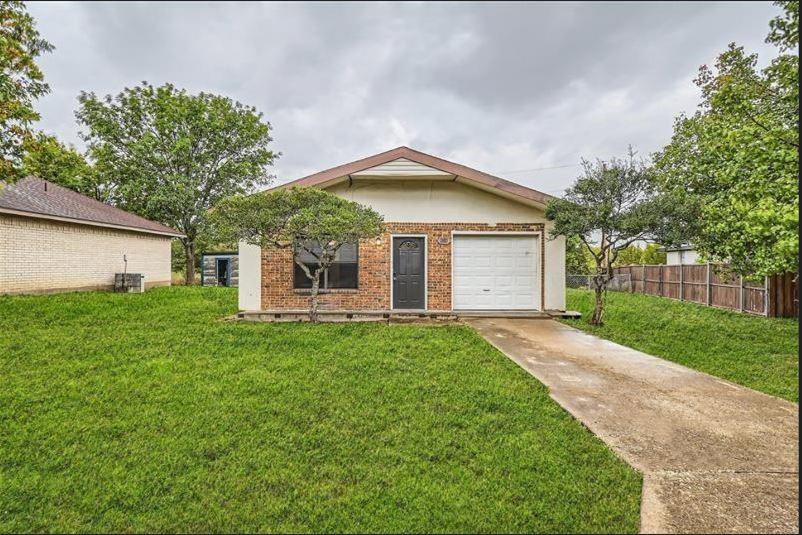 Single-story residence featuring a brick and stucco exterior, concrete driveway, attached garage, and mature trees