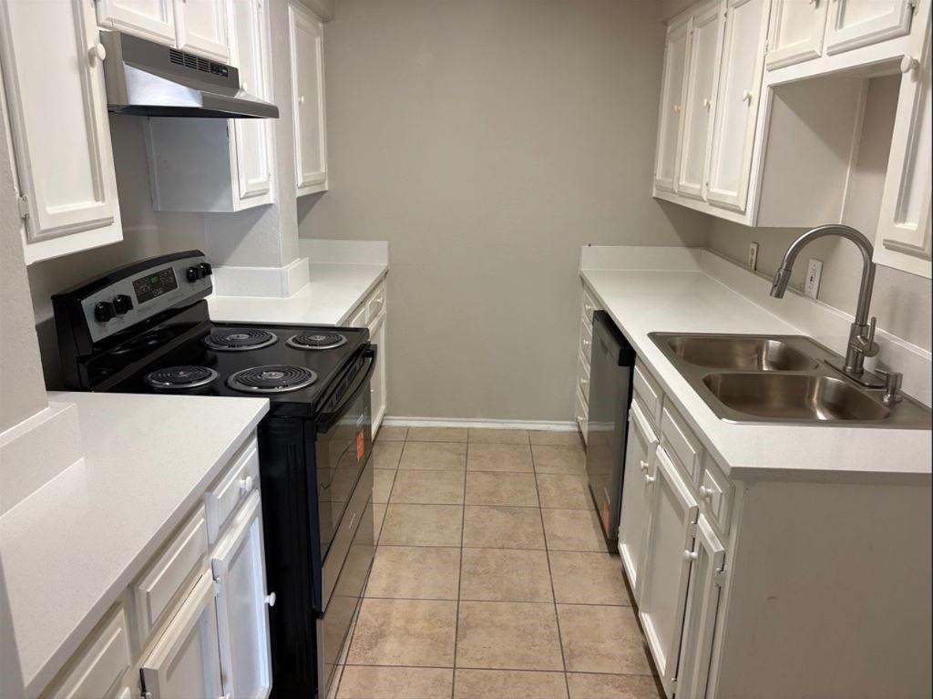 Kitchen featuring white cabinetry, light-toned solid surface countertops, a dual-basin stainless steel sink with a high-arch faucet, black range, and tile flooring