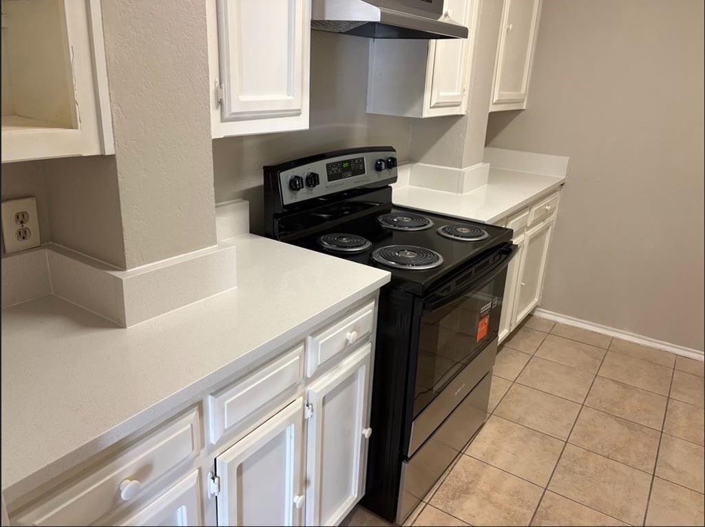 Kitchen featuring white cabinetry, light-toned solid surface countertops, a black electric range, an overhead vent hood, and tiled flooring