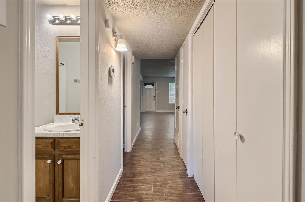 Hallway featuring wood-finish flooring, white bifold closet doors, and a bathroom containing a vanity with a stone-surface countertop, integrated basin, and wood-finish cabinetry