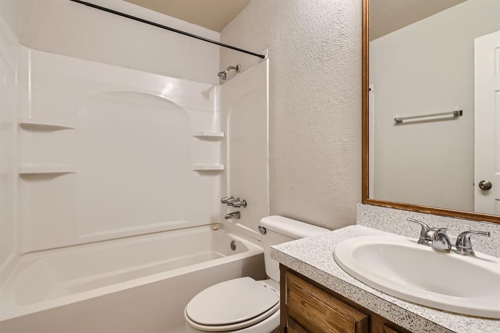 Bathroom featuring a molded composite tub and shower surround with integrated shelving, vanity with a speckled composite countertop, undermount sink, and wood-finish cabinetry