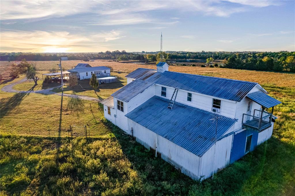 Expansive rural acreage featuring a two-story outbuilding with a metal roof, an elevated wooden balcony, and an additional secondary structure situated on the grounds